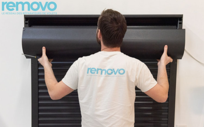 Un technicien de Removo installe ou répare un volet roulant noir.
