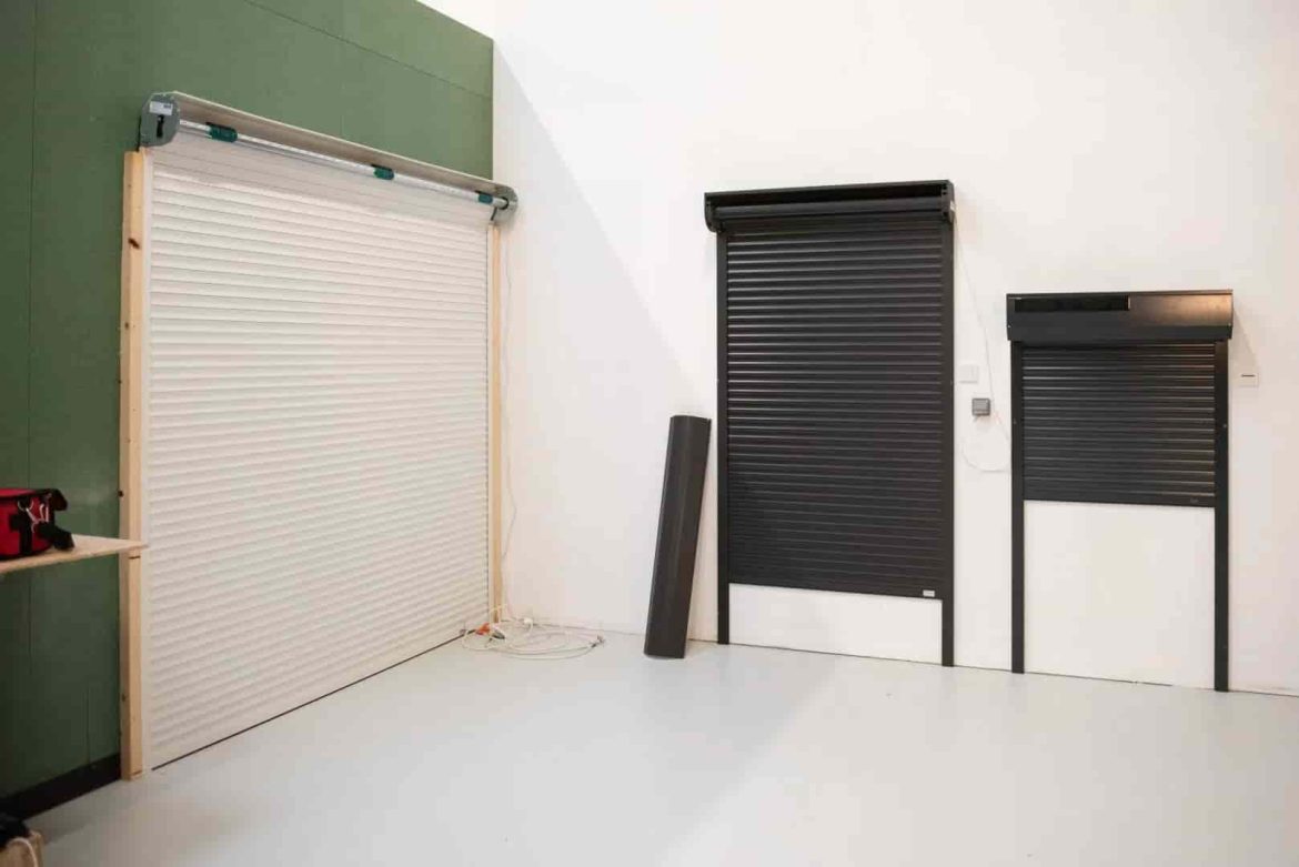 Exposition de trois modèles de volets roulants, un blanc et deux noirs, dans un environnement lumineux.