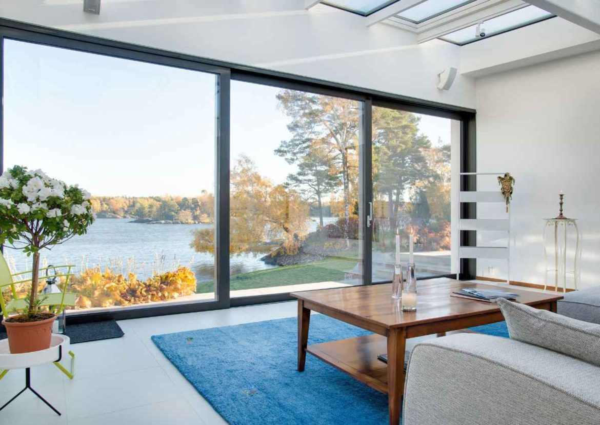Un salon lumineux avec de grandes baies vitrées offrant une vue sur un lac, mettant en valeur les menuiseries contemporaines.