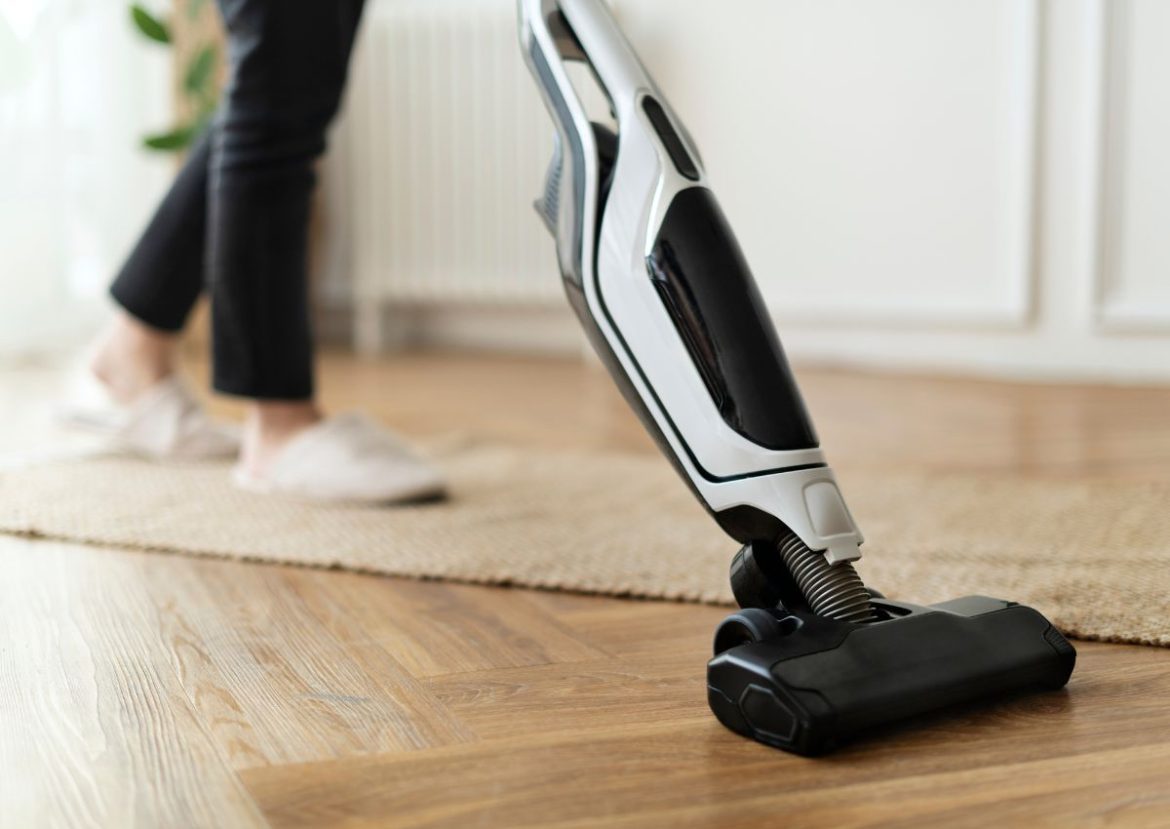 Une personne utilise un aspirateur-balai sans fil pour nettoyer un sol en parquet.