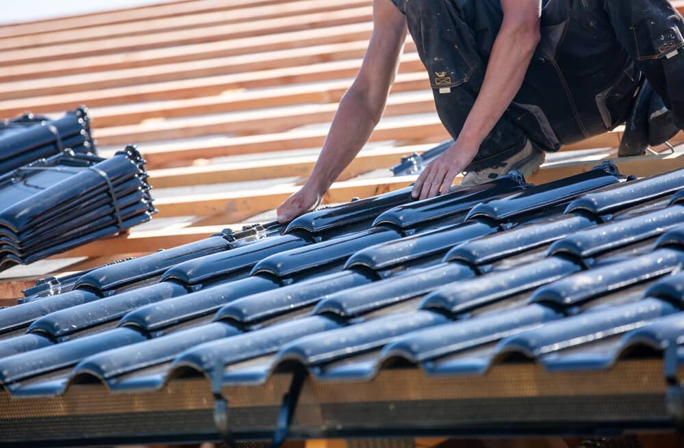 Un ouvrier effectuant des travaux de "rénovation de toiture", remplaçant des tuiles endommagées pour assurer l'étanchéité et la solidité de la maison