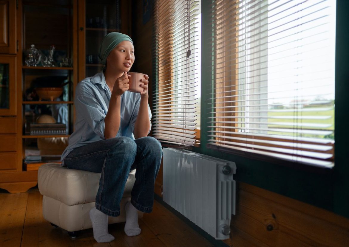Femme avec un store électrique, buvant une boisson chaude et regardant par la fenêtre.