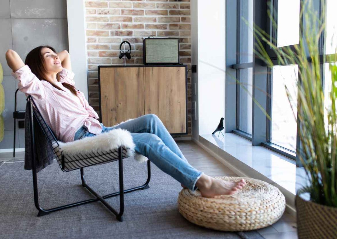 Détente et confort à la maison avec des films solaires. Femme se détendant les yeux fermés dans un fauteuil près d'une grande fenêtre, profitant d'un intérieur protégé des UV grâce à des films solaires.