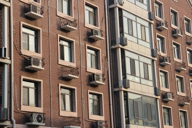 Façade d'immeuble résidentiel en briques avec de nombreuses fenêtres, balcons en fer forgé et climatiseurs, mettant en avant le besoin de fenêtres modernes avec isolation thermique.
