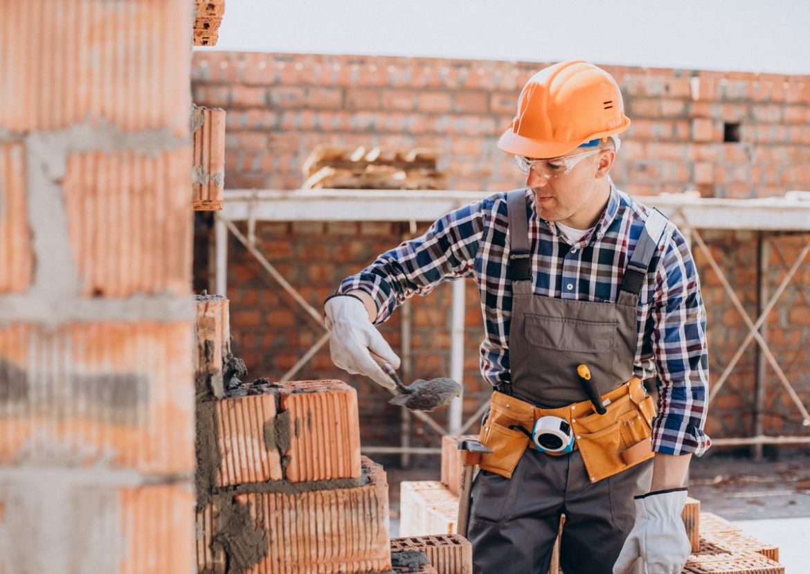 Maçon professionnel en train de poser des briques sur un chantier de construction de maison.