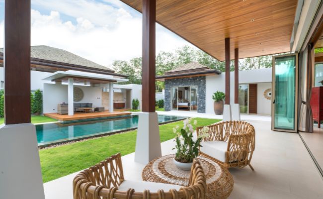 Terrasse couverte avec mobilier en rotin, piscine et villa moderne, soulignant la qualité de la menuiserie sur mesure du plafond.