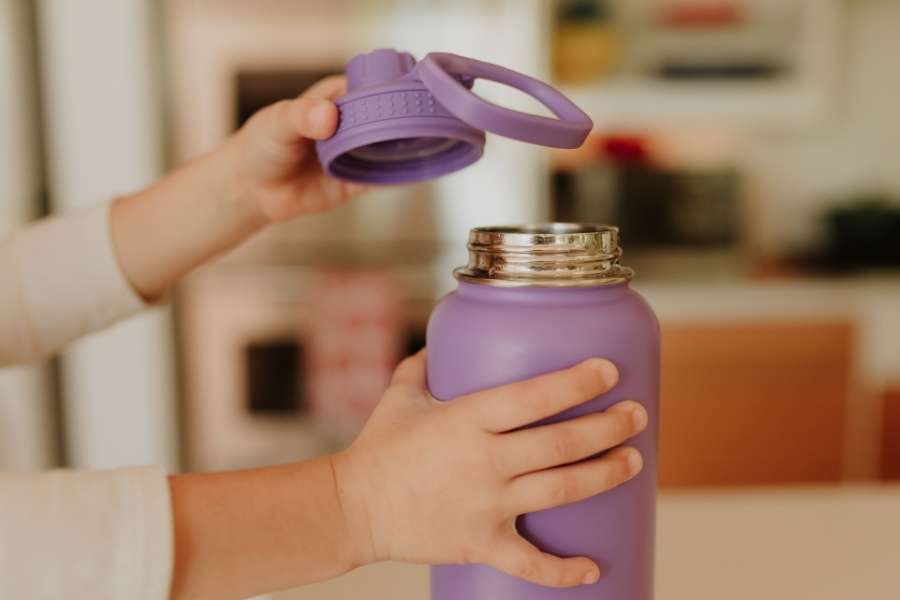 Les mains d'un enfant ouvrent une gourde filtrante violette à l'intérieur d'une maison.