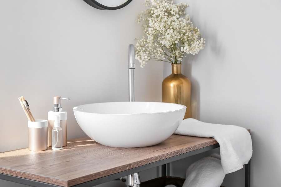 Éclairage salle de bain naturel et doux sur un meuble vasque en bois avec une vasque ronde et des accessoires dorés.
