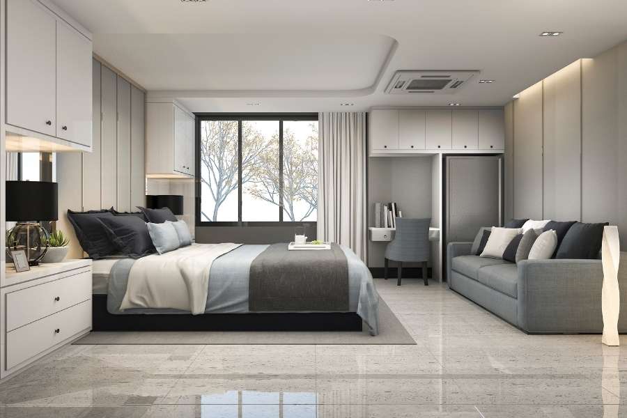 Une chambre à coucher moderne avec un lit gris, un canapé et un espace bureau intégré, le tout dans des tons neutres.