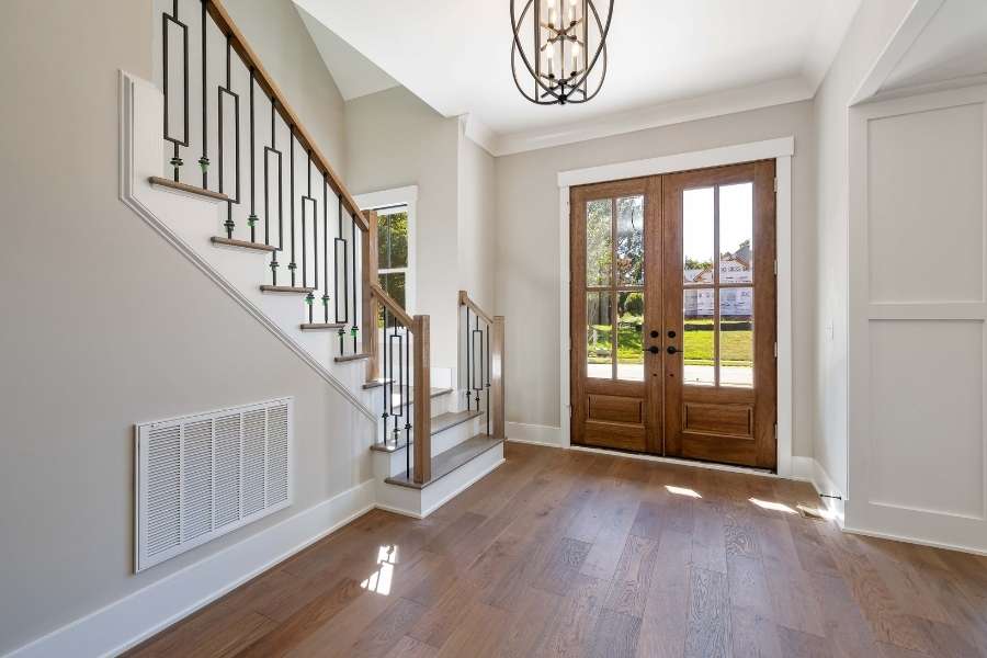 Hall d'entrée avec un escalier et une double porte d'entrée en bois qui semble coincée.