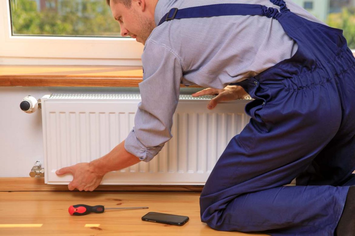 Un technicien en combinaison bleue intervient sur un radiateur blanc pour comment optimiser rendement installation chauffage.